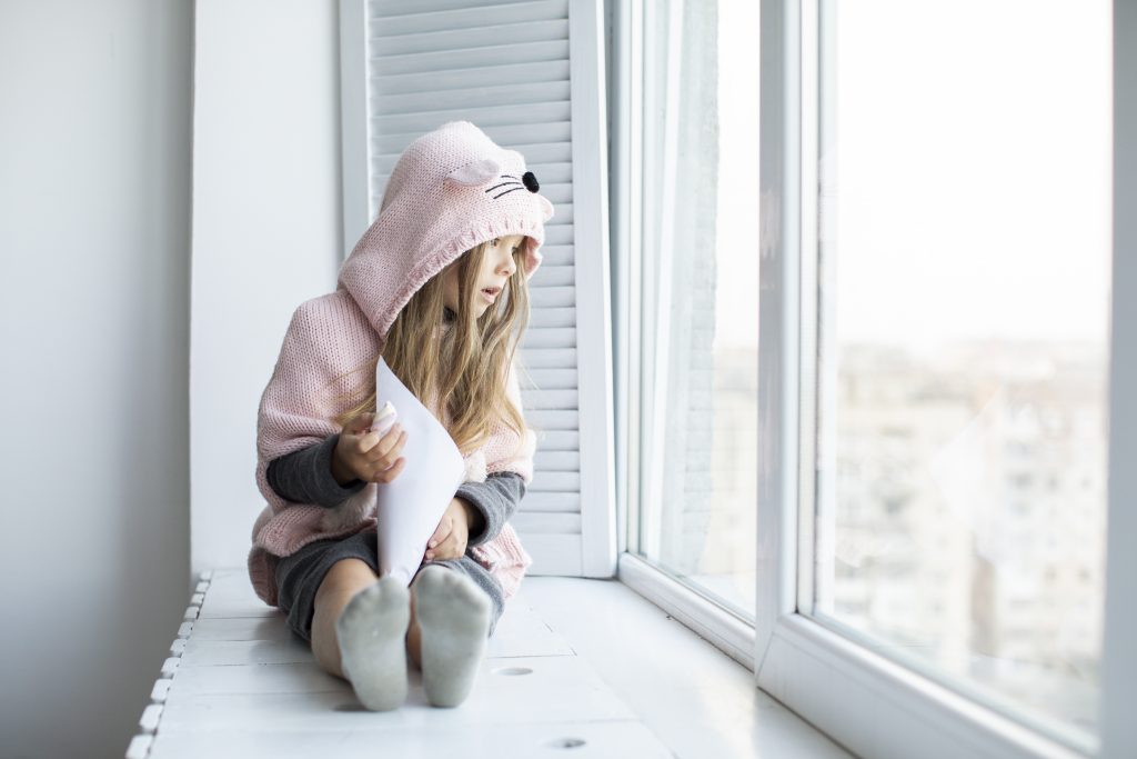 Little girl sat in a bay of a window looking outside