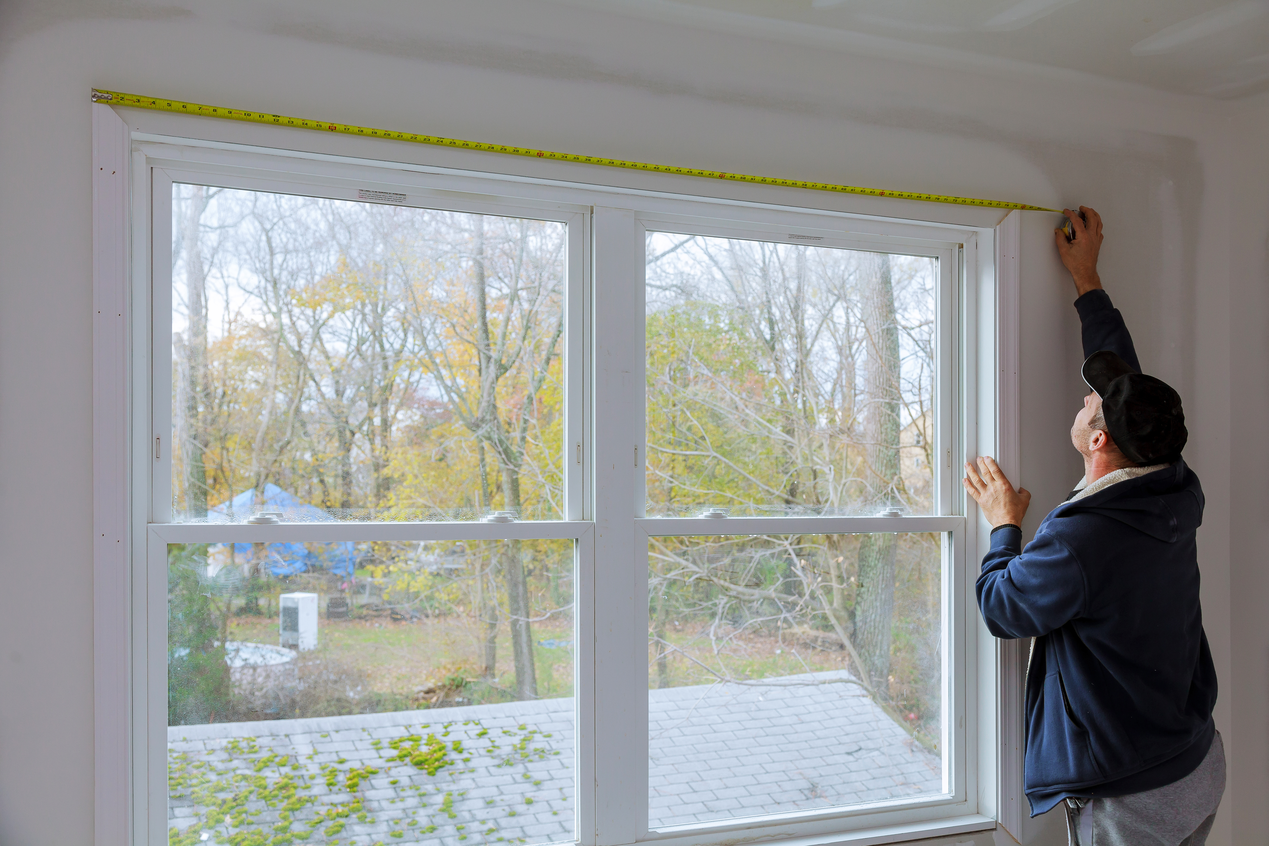 Man using measuring tape to measure the size of a window.