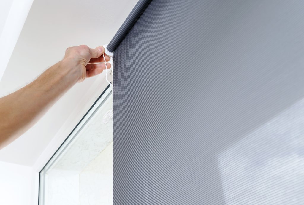 Man's hand is puting a roller blind to a window.